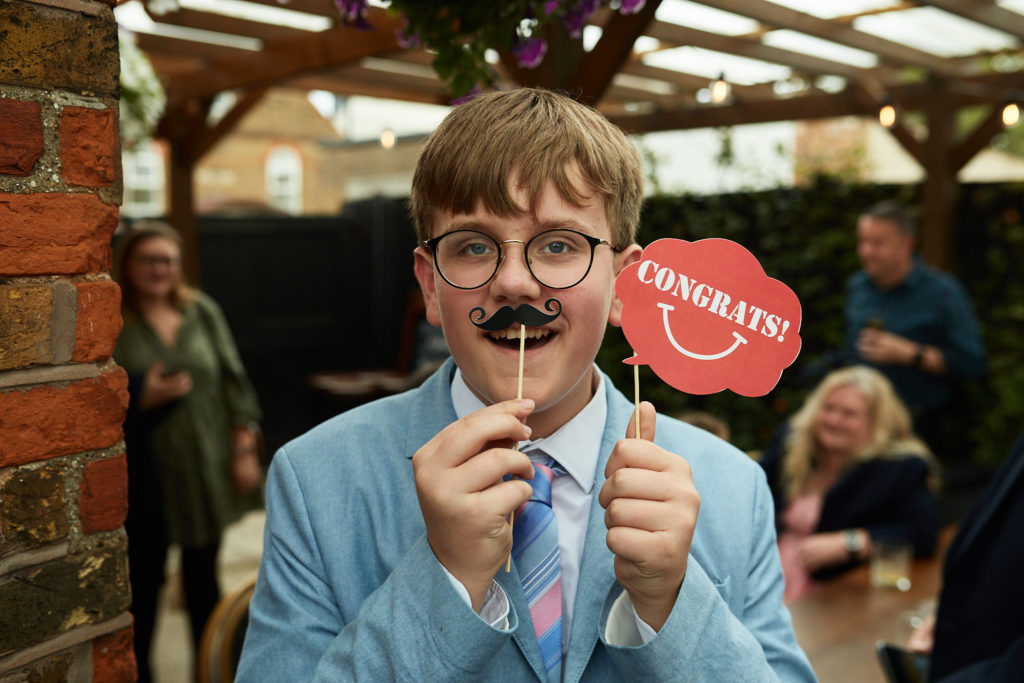 Guest in a light blue suit holding up moustache and "Congrats" photo props