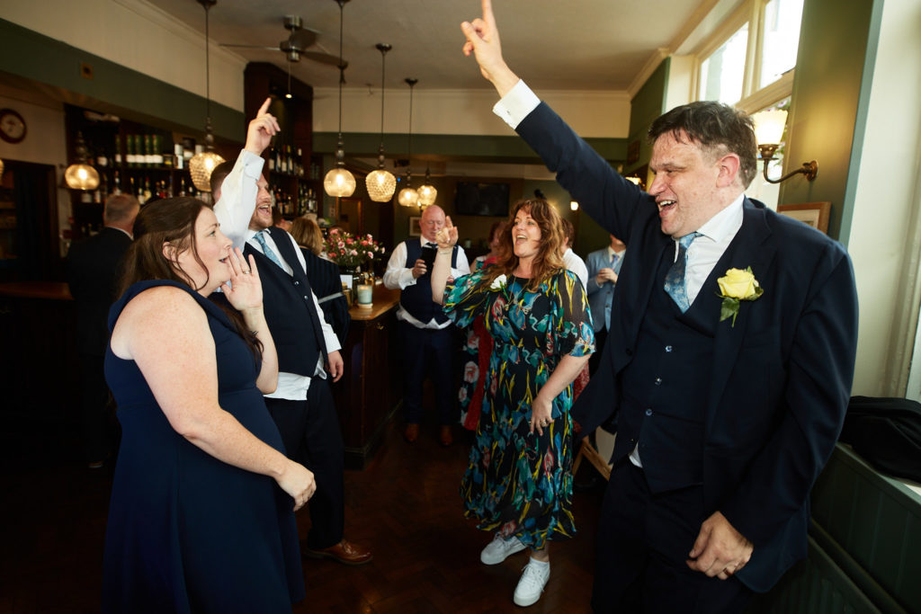 Groom dancing with his arm in the air among guests
