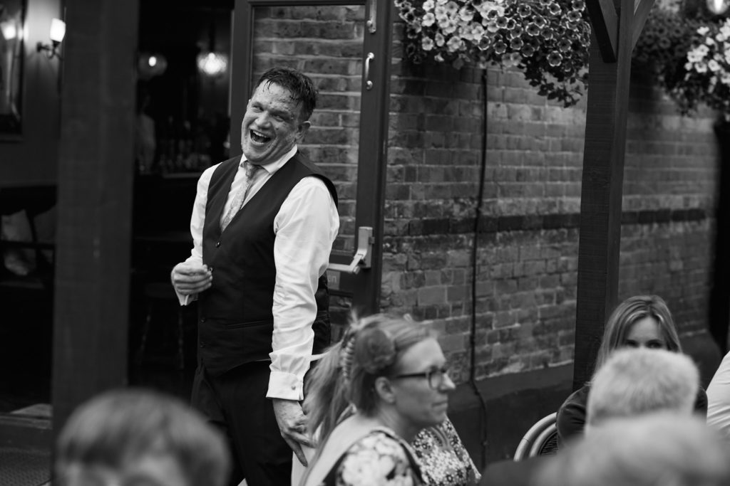 Black and white photo of a groom laughing under festoon lights in the garden