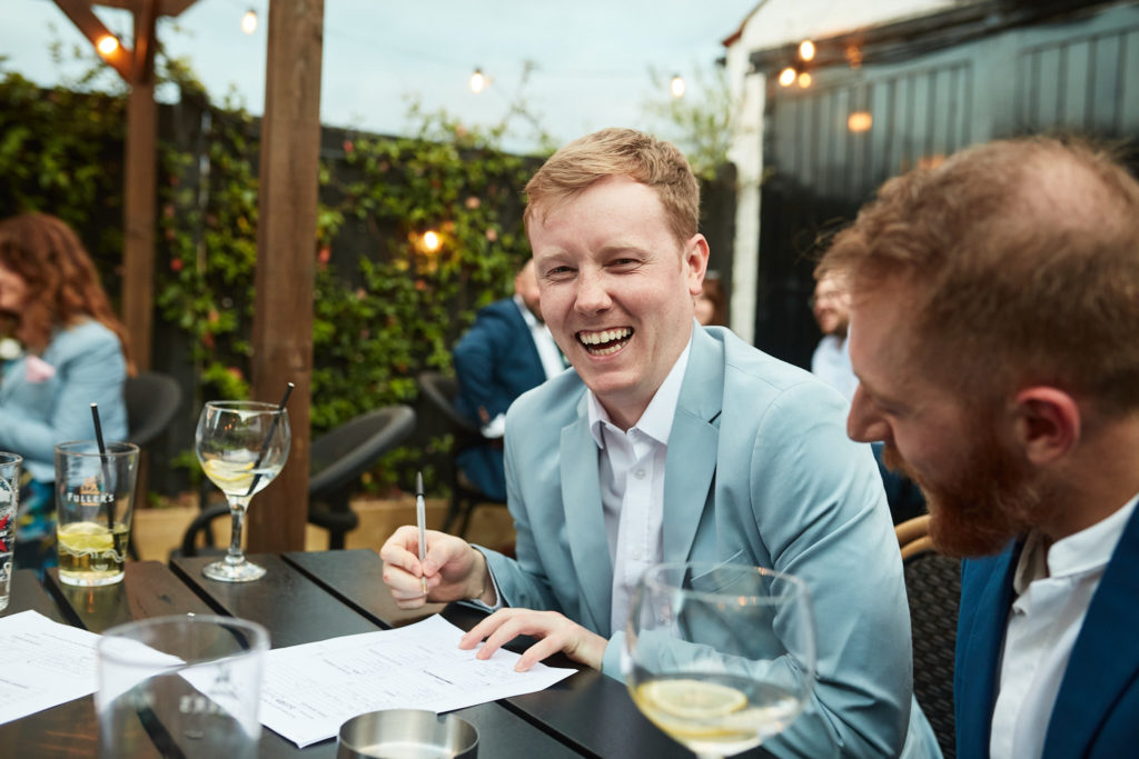 Guest in a light blue suit writing at the table during the wedding pub quiz