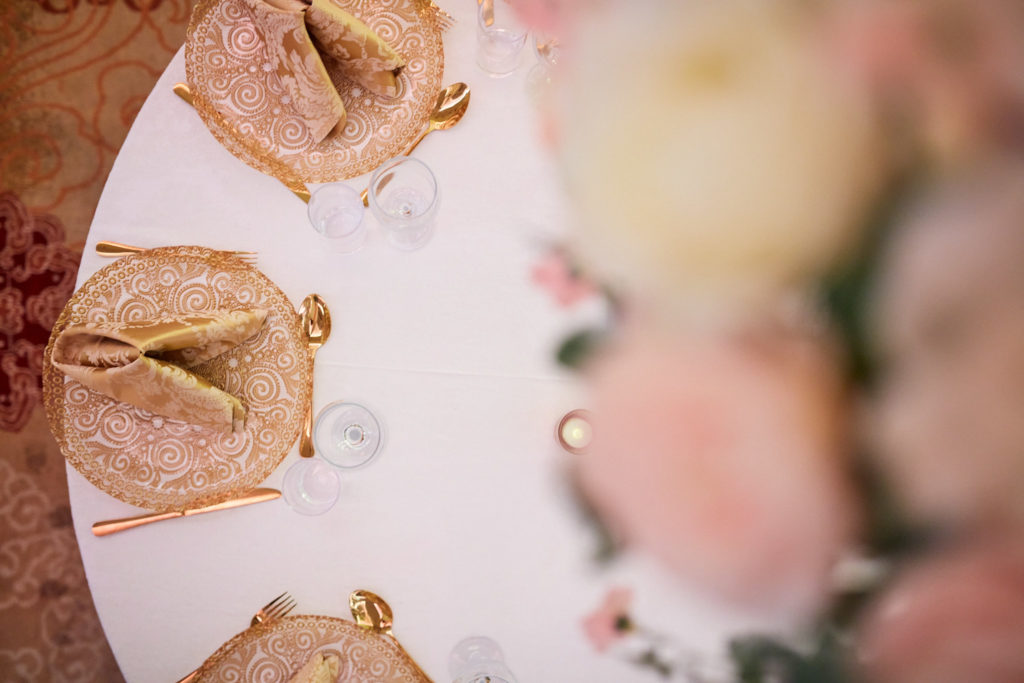 Gold napkins on a round table with blush flowers, seen from above