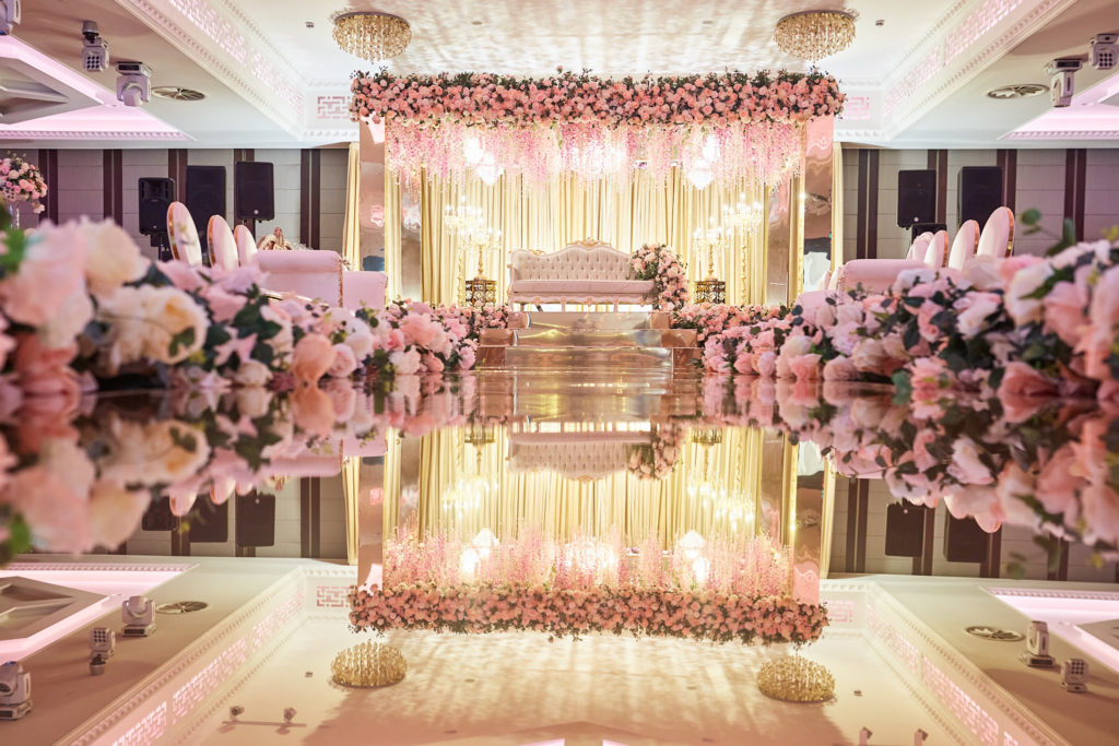 Wedding stage with a flower canopy and gold drapes reflected in a mirrored aisle