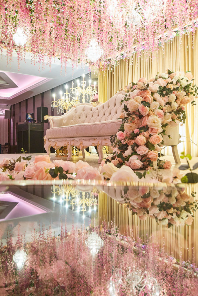 Stage sofa beneath hanging pink blossom and chandeliers, reflected in the mirrored floor