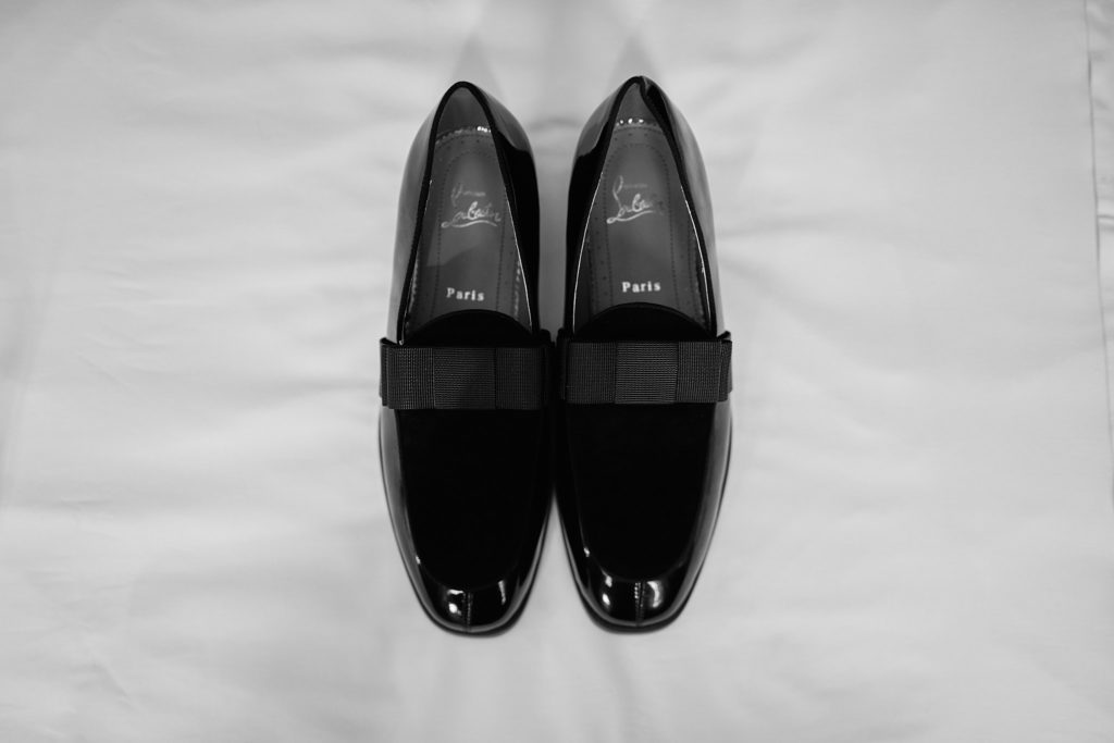 Groom's black velvet loafers on a white bed