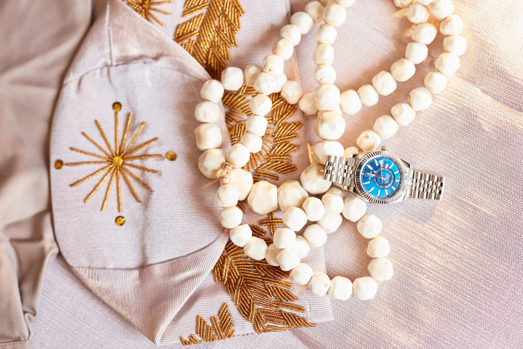 Coral bead necklace and a blue-faced watch on embroidered cream fabric