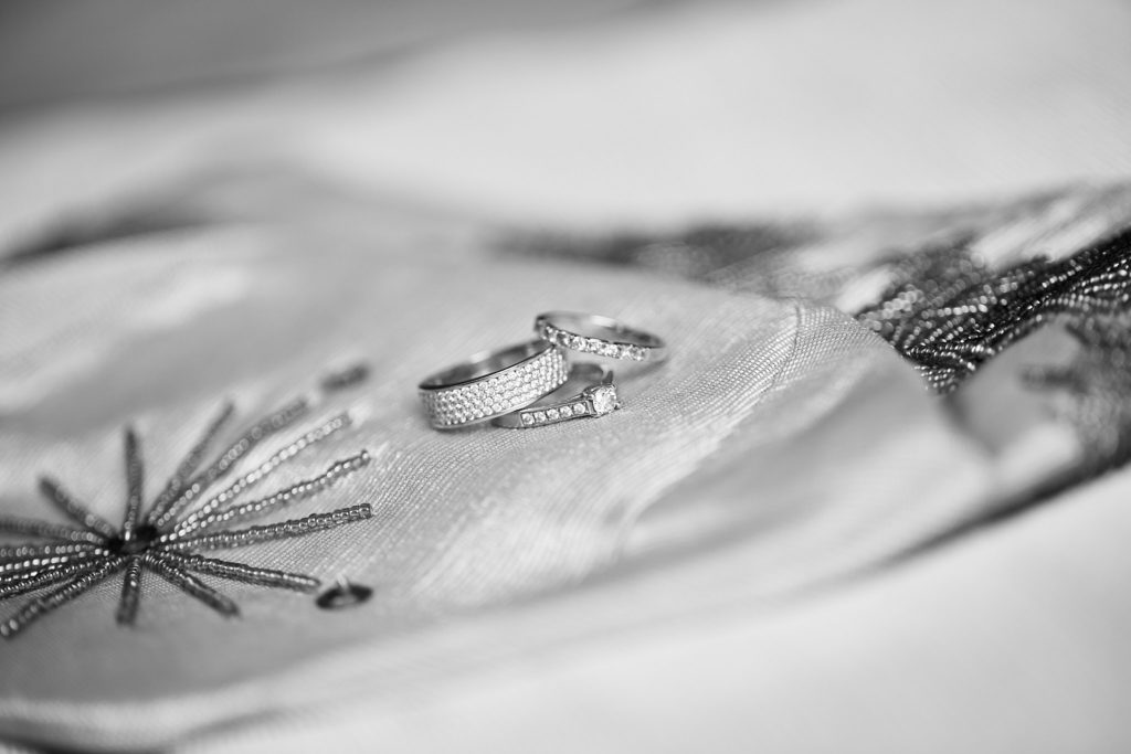 Black and white photo of wedding rings on embroidered fabric