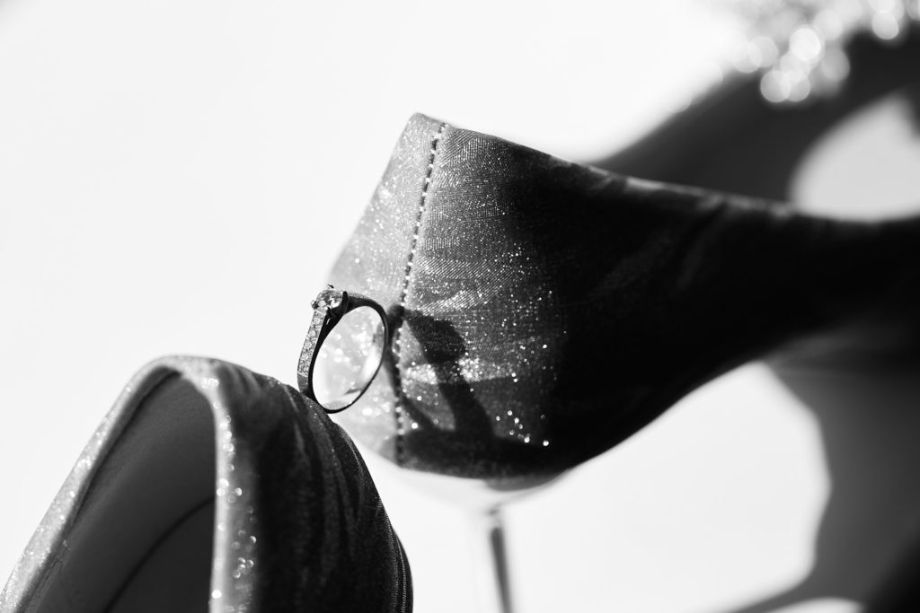 Black and white close-up of a ring balanced on the heel of a bridal shoe