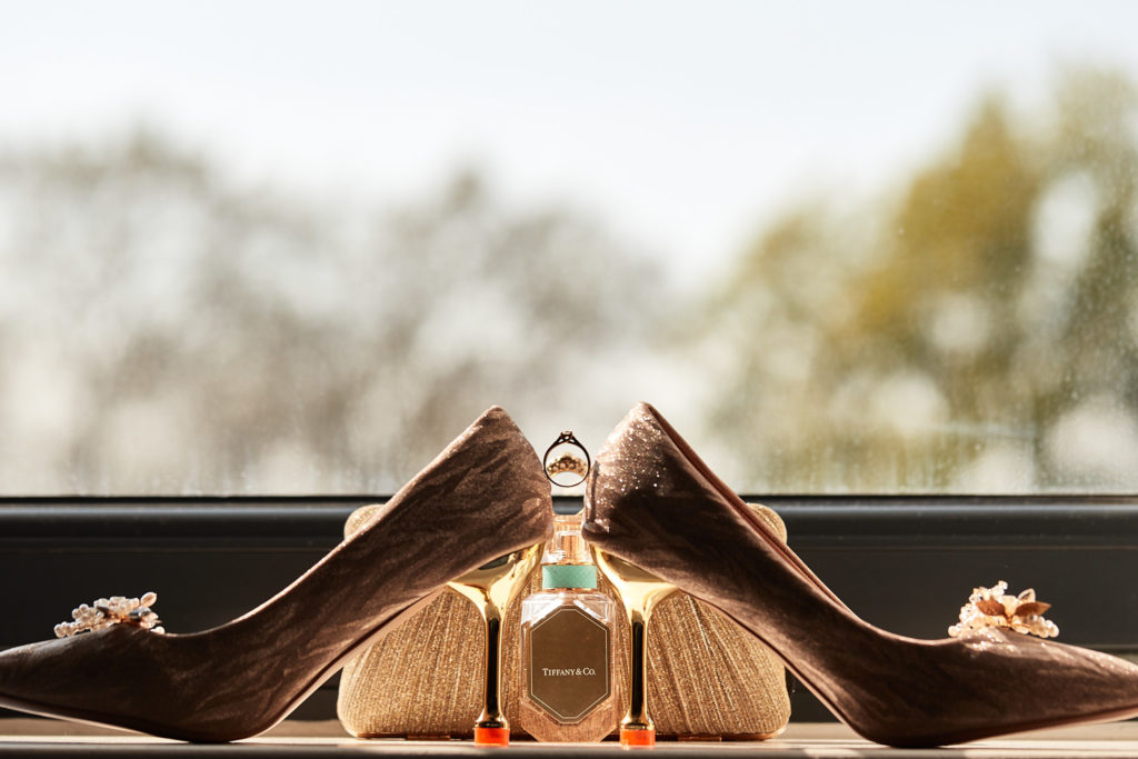 Jewelled bridal shoes with a bottle of perfume between them on a windowsill