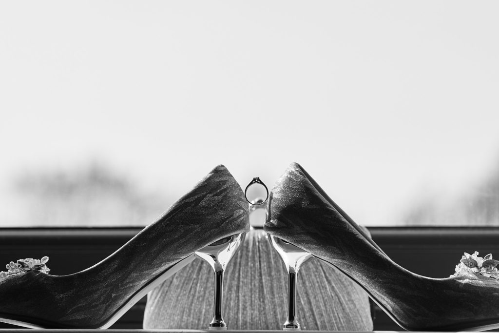 Black and white photo of bridal shoes and a perfume bottle on a windowsill