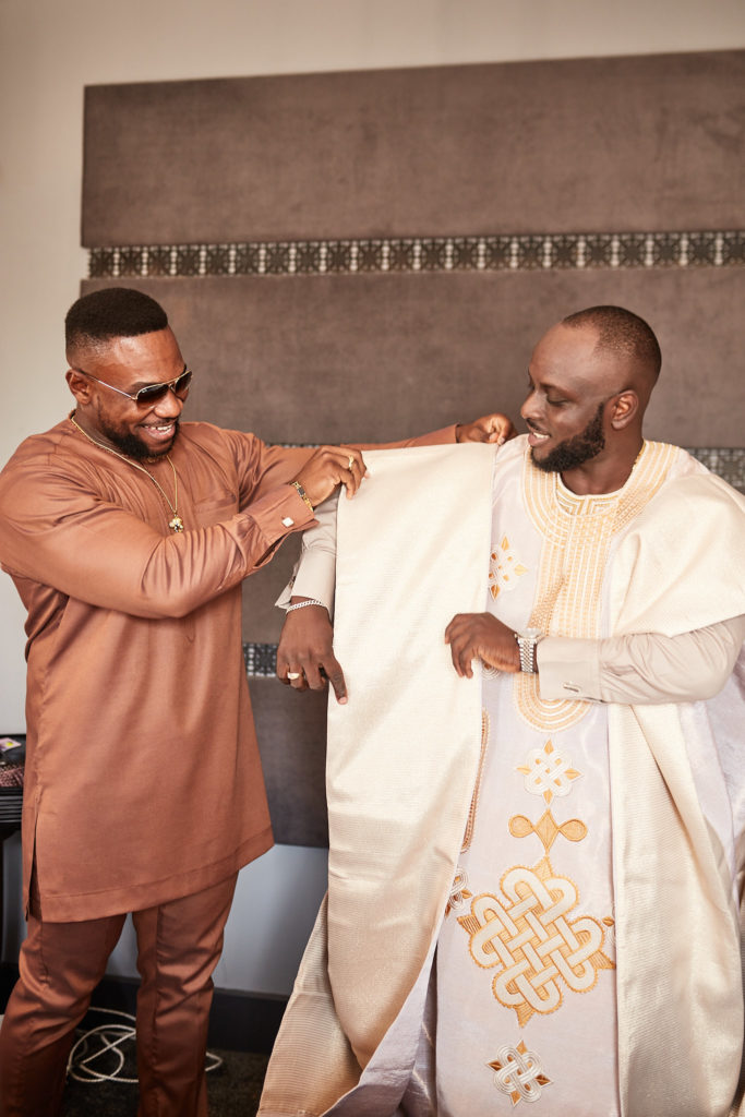 Groomsman helping the groom into his cream embroidered robe