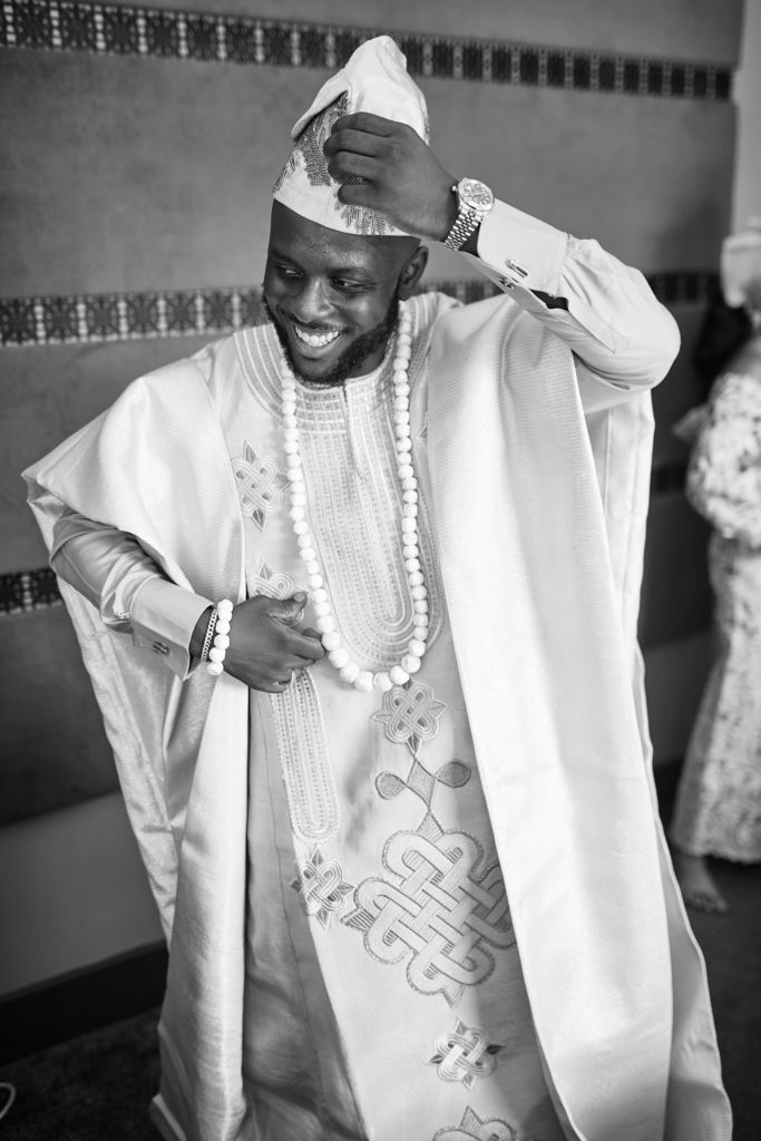 Black and white photo of the groom smiling as he adjusts his cap in traditional robes