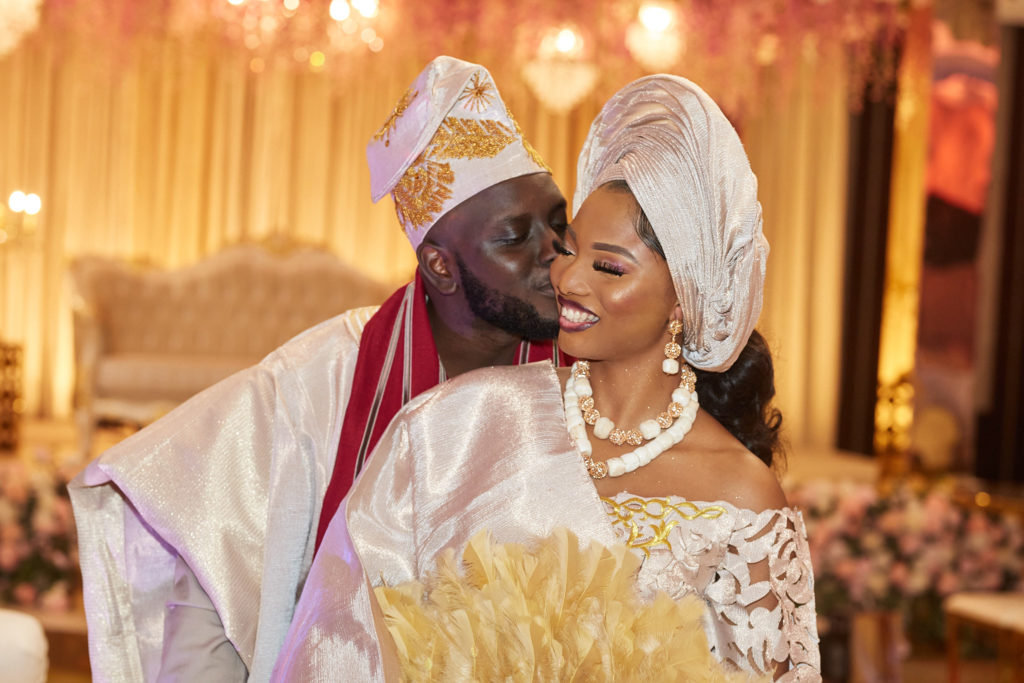 Groom kissing the bride's cheek as she holds a gold feather fan