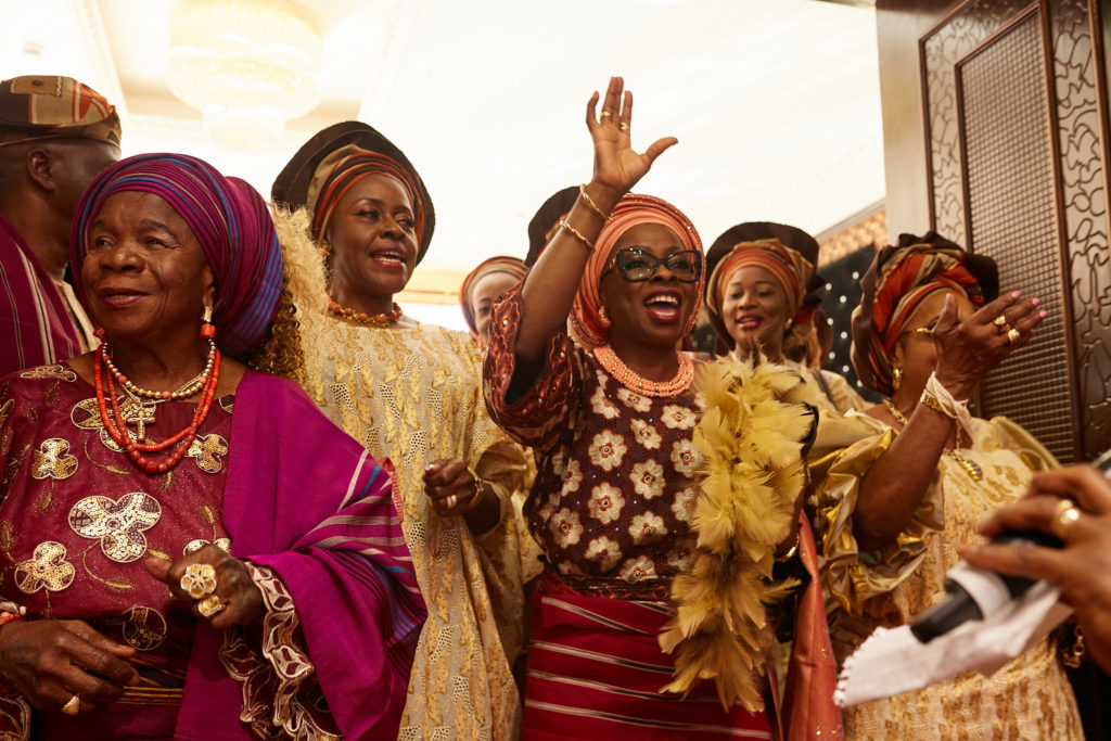 Women in matching head ties and coral beads dancing into the wedding
