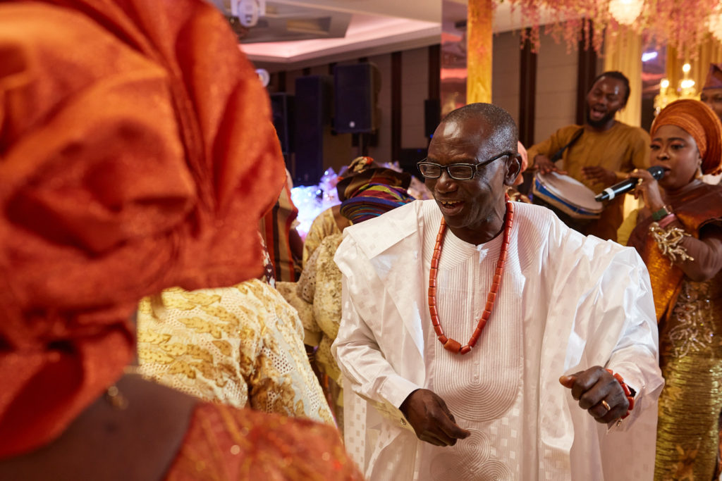 Older man in white traditional dress and coral beads dancing among the guests