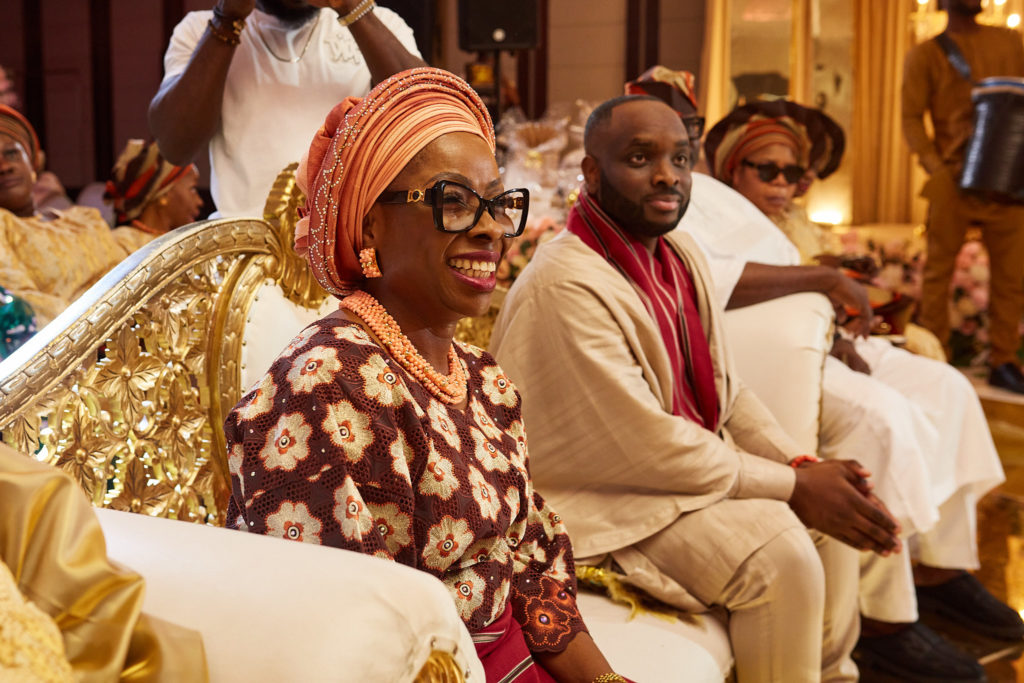 Guest in sunglasses and a coral head tie smiling as she sits with family