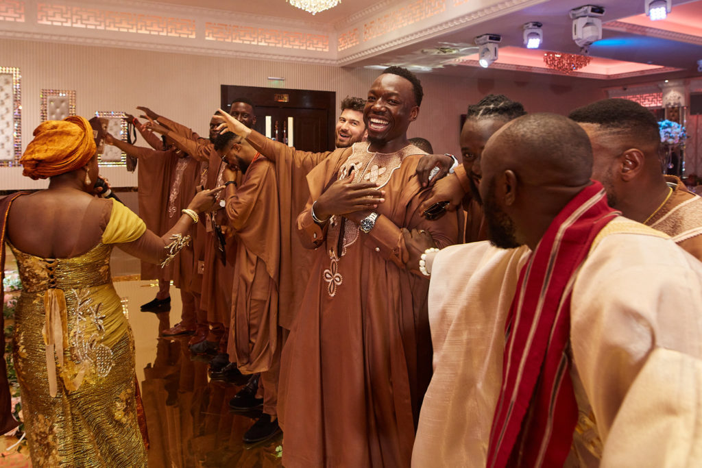 Groom and groomsmen in matching brown outfits dancing into the hall