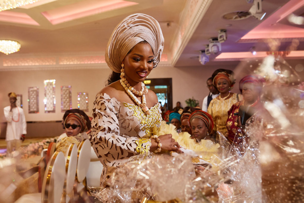 Bride in a cream head tie and gold embroidered outfit seated during the ceremony