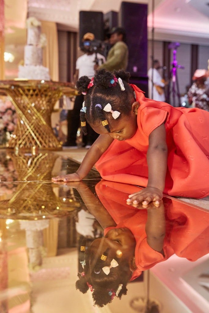 Toddler in an orange dress looking at her reflection in the mirrored floor