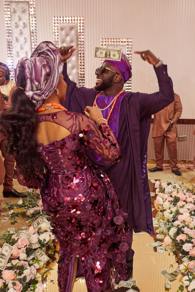 Bride and groom dancing in purple sequinned outfits, the groom with a banknote on his forehead