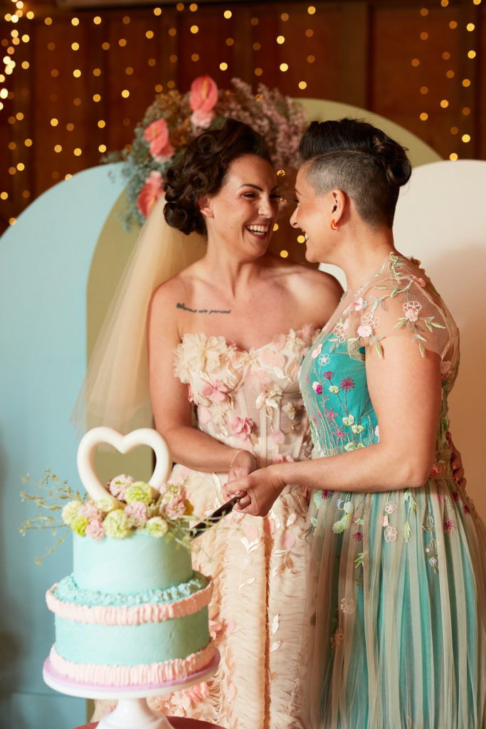 Two brides laughing forehead to forehead as they cut their wedding cake
