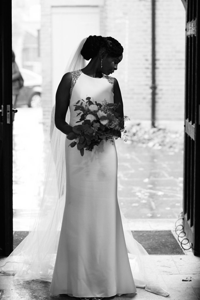 Black and white photo of the bride in a doorway looking down at her bouquet