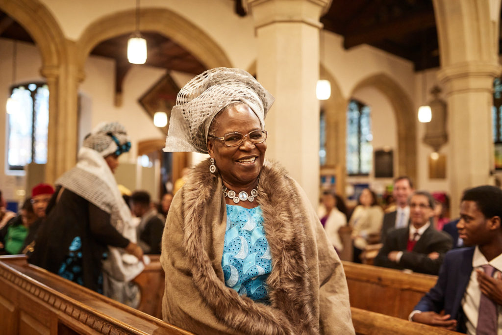 Older guest in a head tie and fur stole smiling as she arrives in church