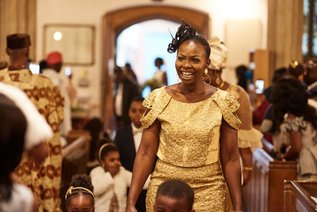 Woman in a gold dress smiling as she walks down the aisle
