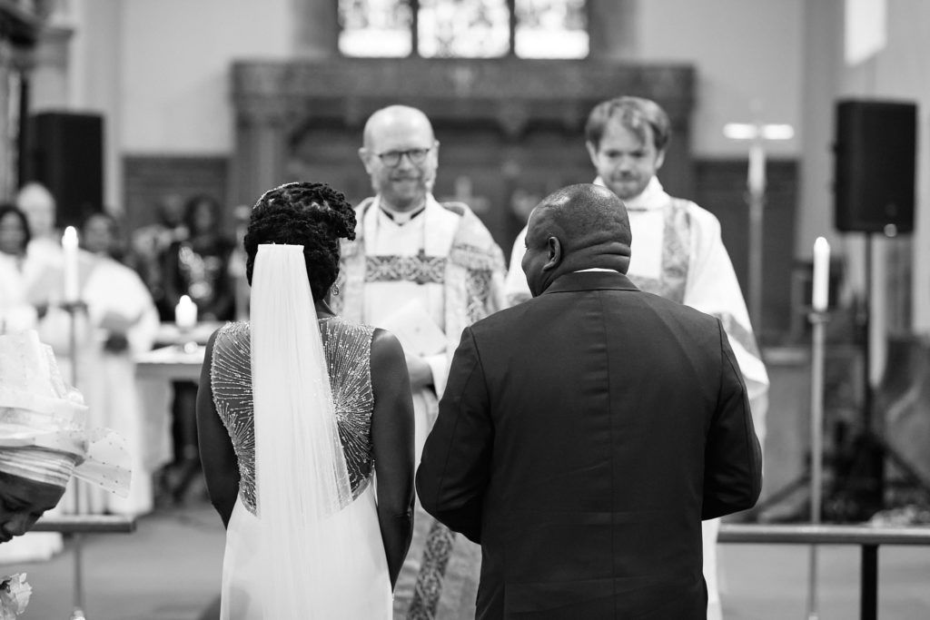 Black and white photo of the bride and groom standing before the clergy