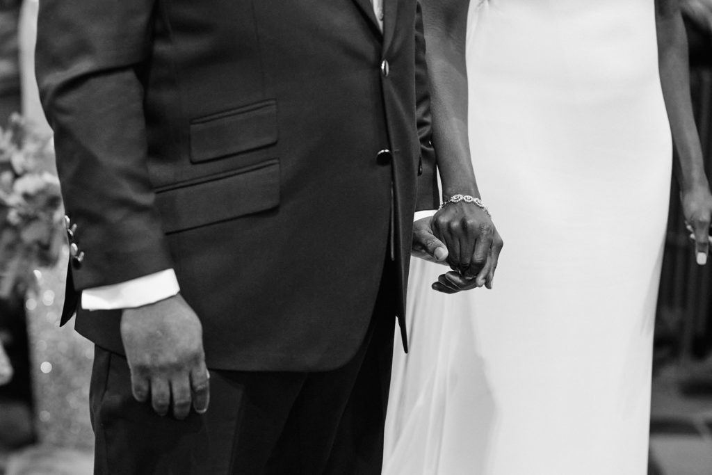Black and white close-up of the bride and groom holding hands