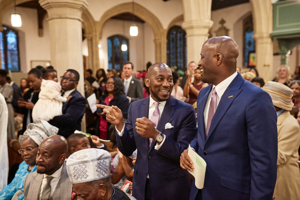 Groom and groomsman smiling as guests gather after the ceremony