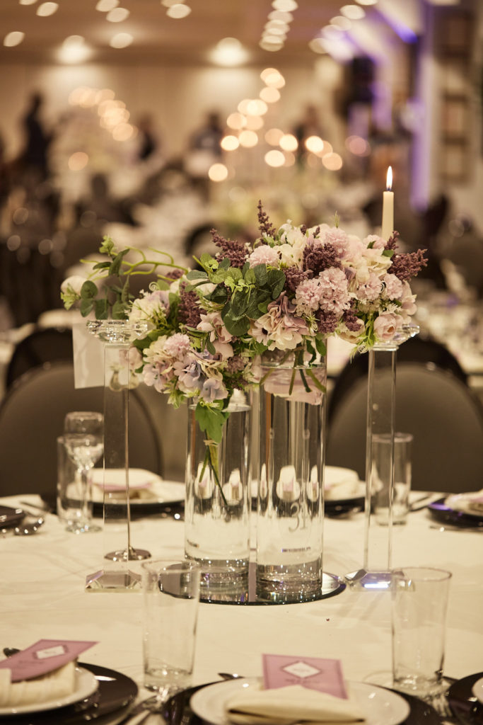 Tall vase of lilac flowers on a wedding table with purple napkins