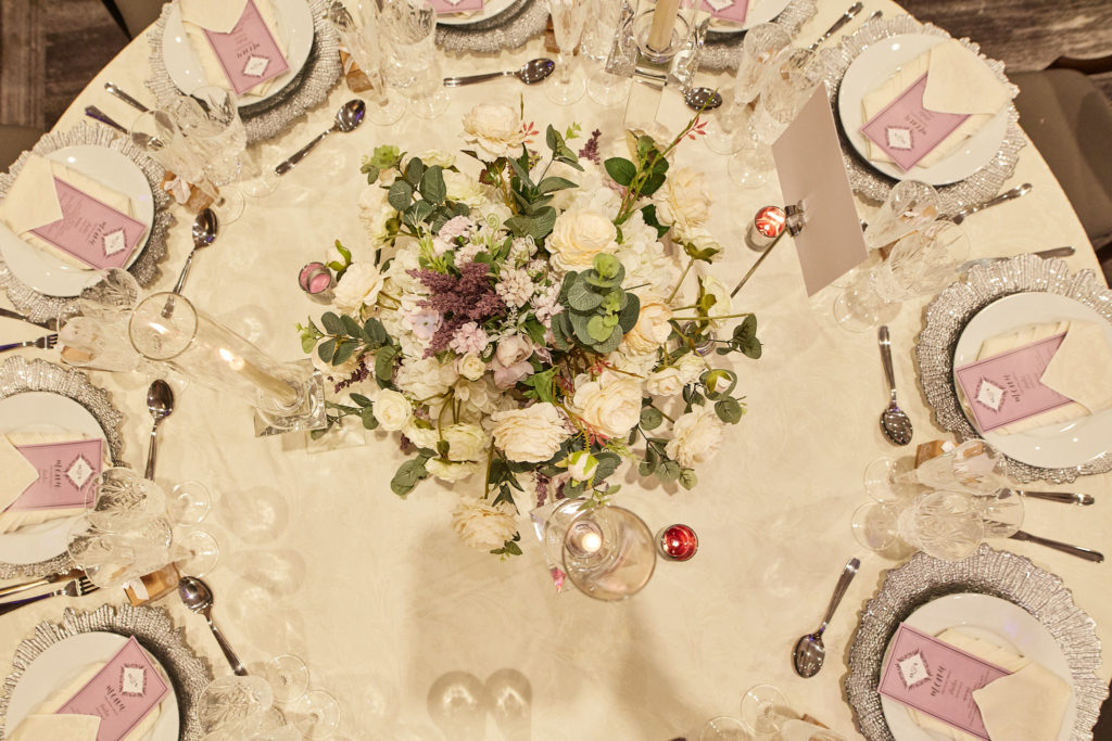 Round table with a floral centrepiece and purple place cards, seen from above