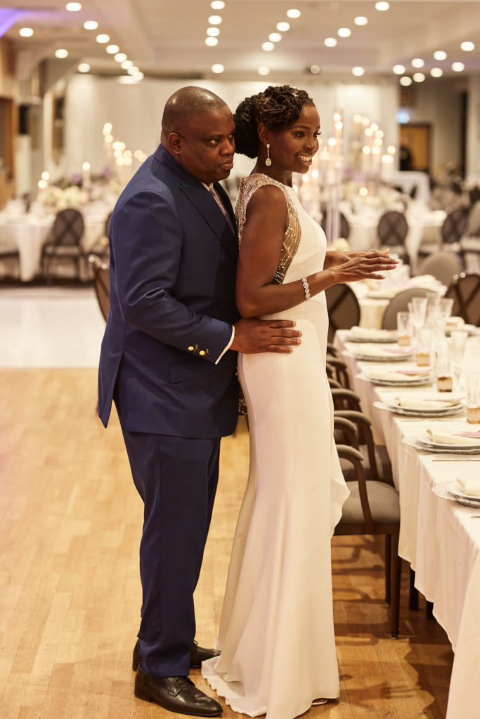 Groom holding the bride from behind as they look over the reception room
