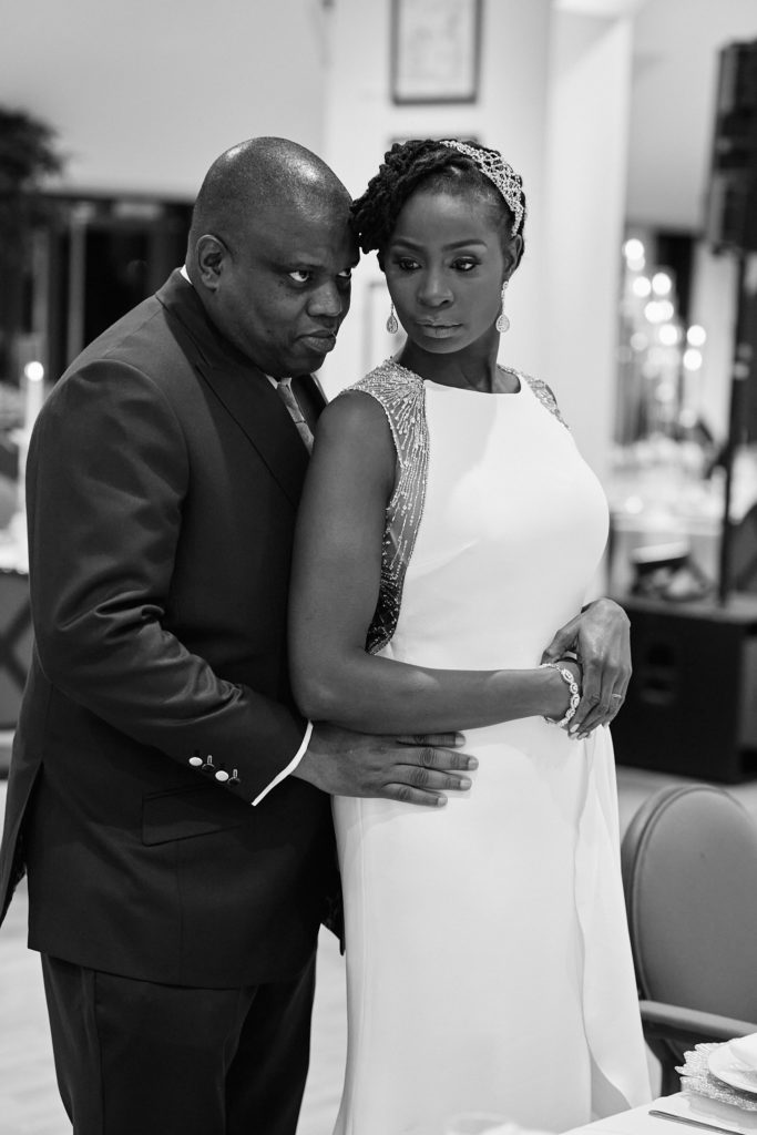 Black and white photo of the groom embracing the bride beside the tables