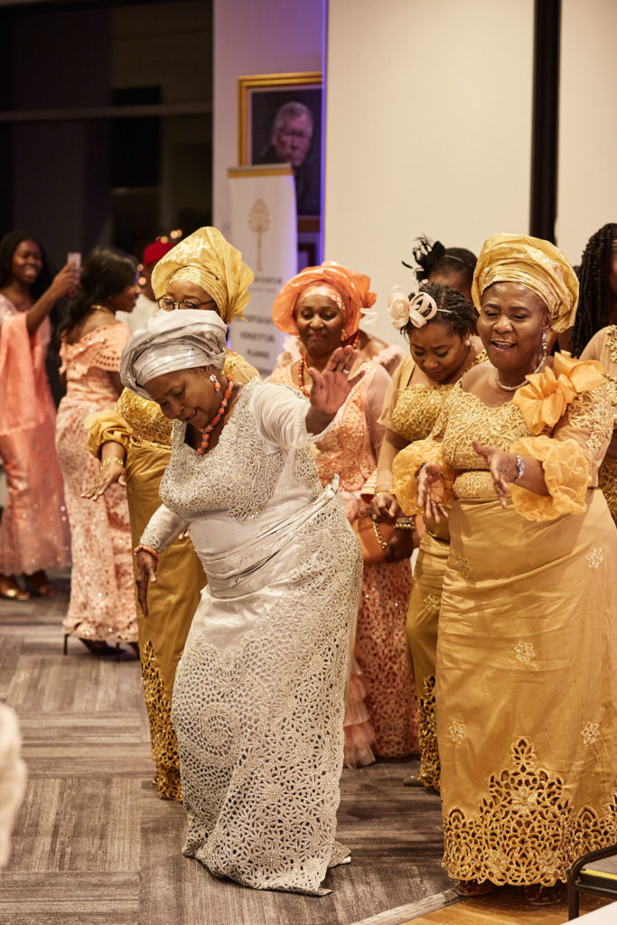 Women in matching gold lace outfits and head ties dancing into the reception