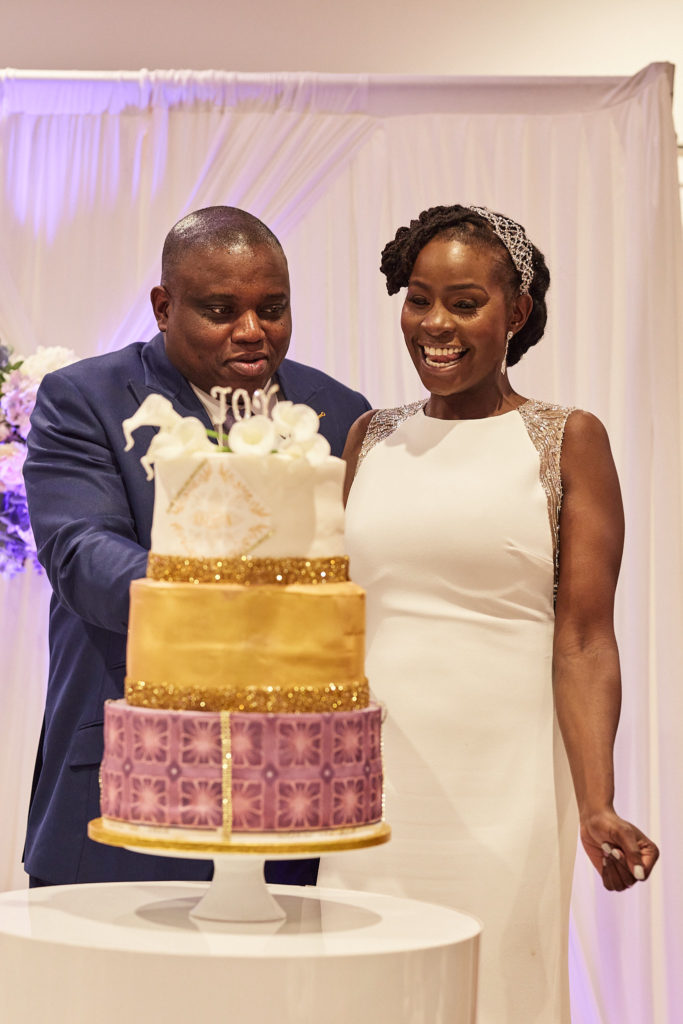 Bride and groom laughing beside their gold and purple wedding cake