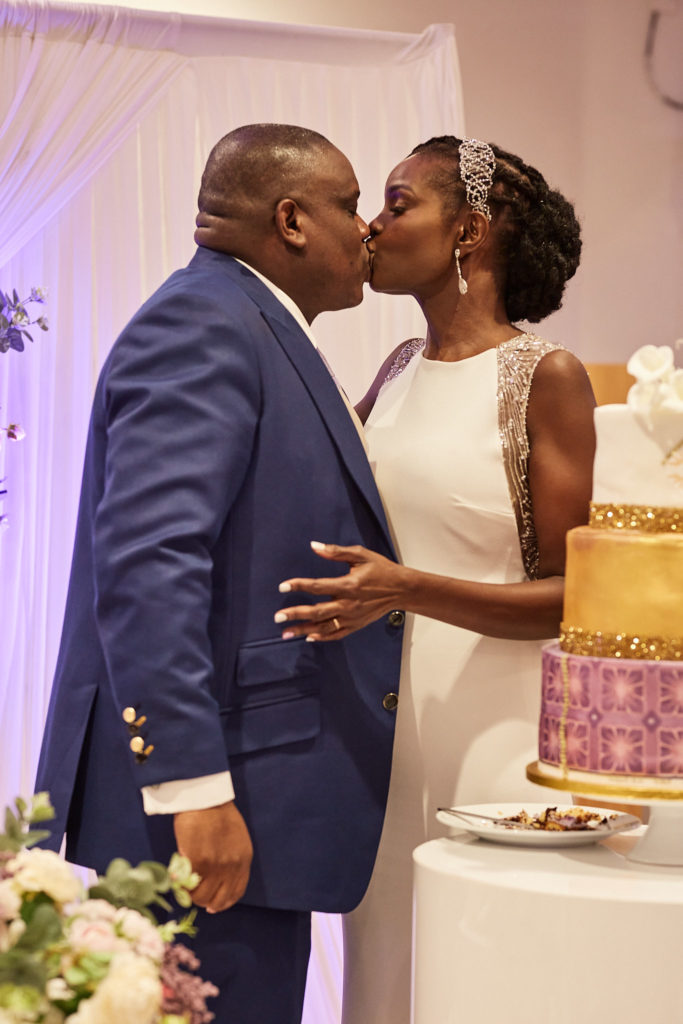 Bride and groom kissing beside their wedding cake