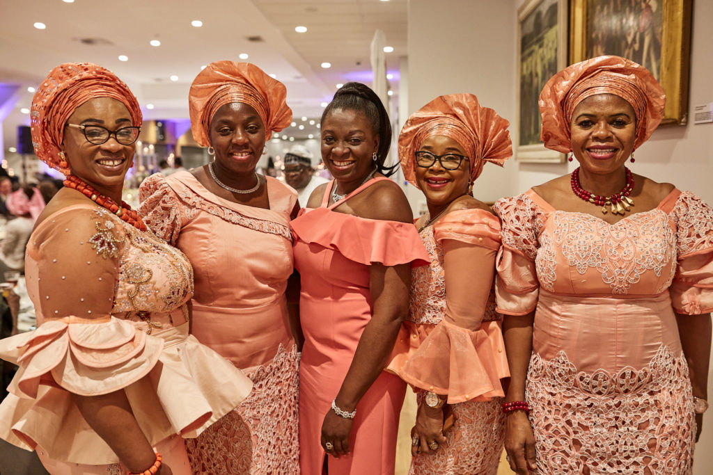Five women in matching coral lace outfits and head ties