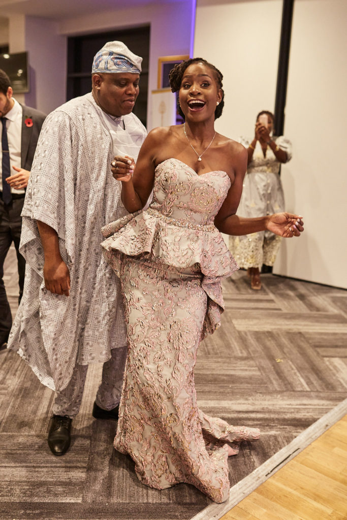 Bride in a blush lace outfit dancing beside the groom in white traditional robes