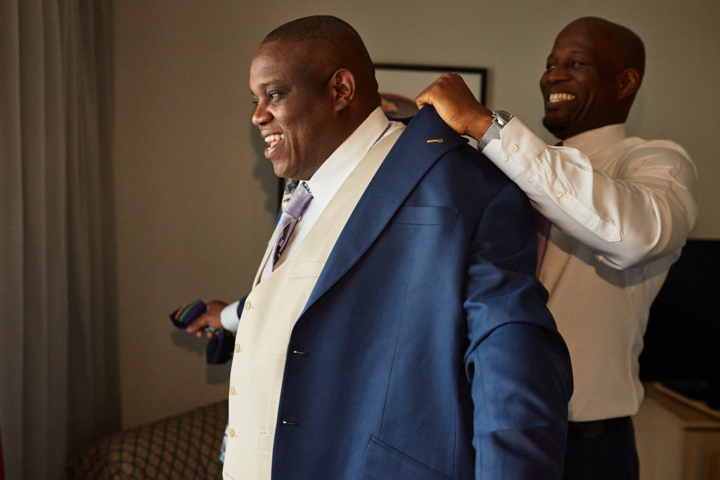 Groomsman helping the groom into his navy jacket