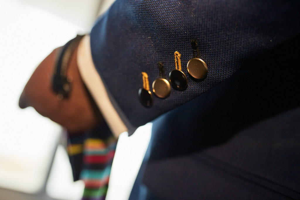 Close-up of the groom's jacket cuff buttons as he adjusts his tie